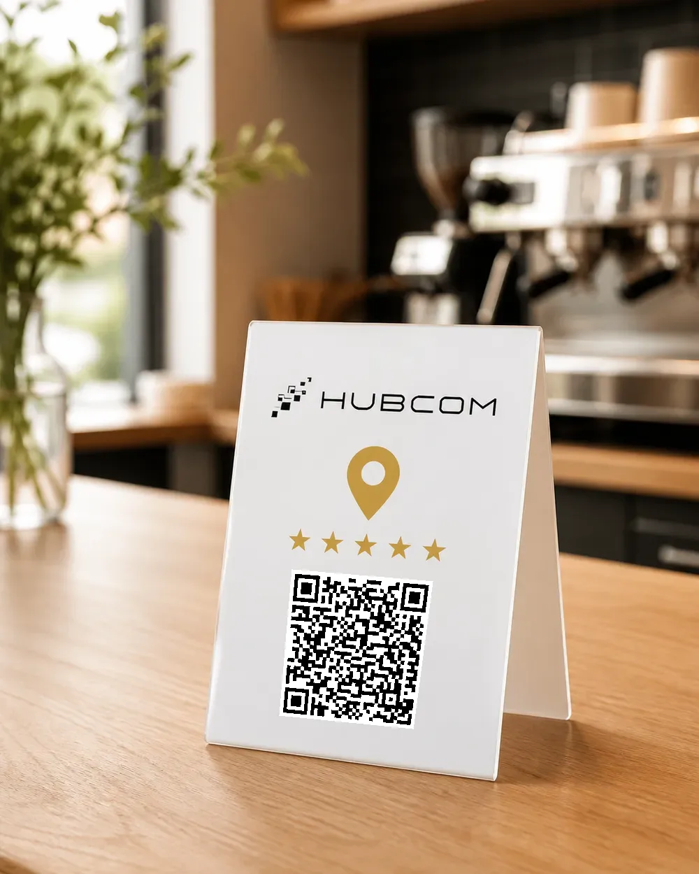 Standee mica trắng dựng trên quầy gỗ quán cà phê, mặt trước in logo Hubcom, ghim bản đồ vàng, năm ngôi sao và mã QR quét được dẫn tới trang đánh giá